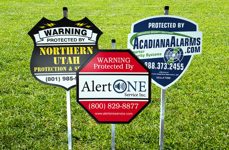 Three yard signs from different home alarm monitoring companies on a lawn