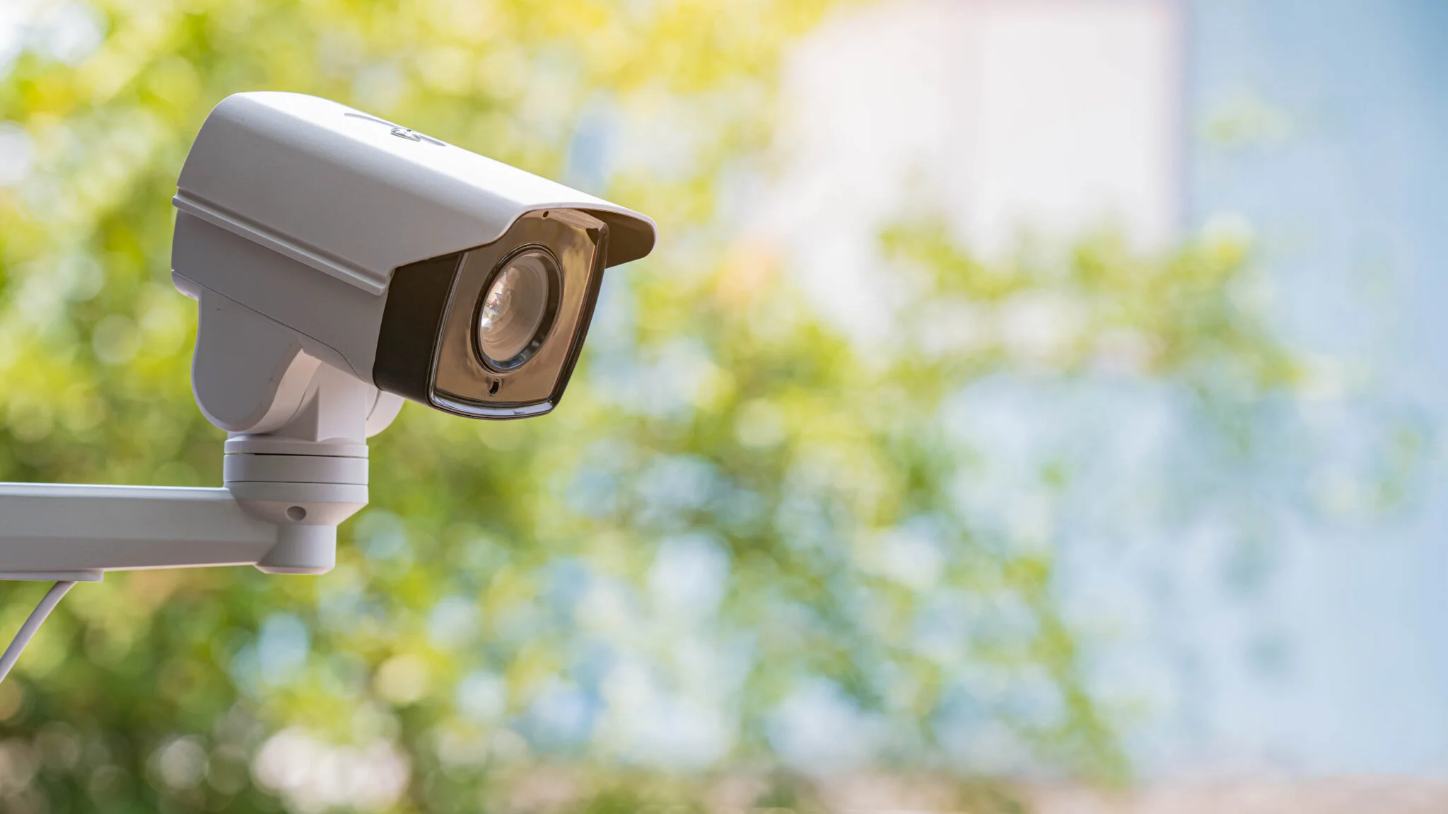 White outdoor security camera mounted against a green garden backdrop