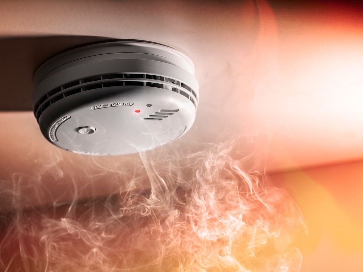 Smoke detector on a ceiling with smoke rising toward it
