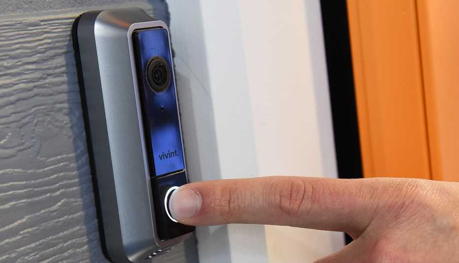 Finger pressing the button on a video doorbell mounted beside a door
