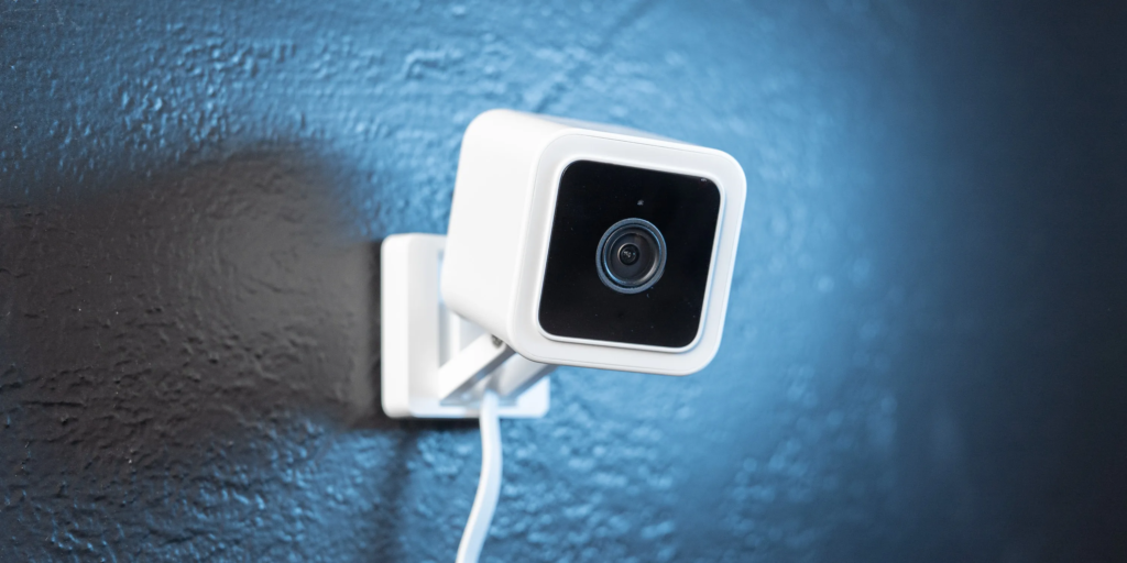  A Wyze Cam v3, designed as a compact Motion Detector Home Security Cameras is mounted on a wall with a smooth blue surface.